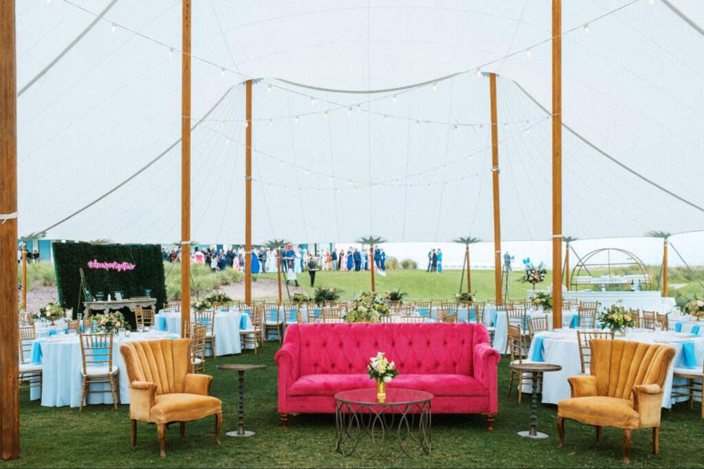 A summer time wedding under a sailcloth tent with tables and chairs and lounge seating