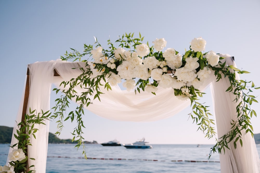 Fragment of a wedding arch decorated with white tulle and flowers