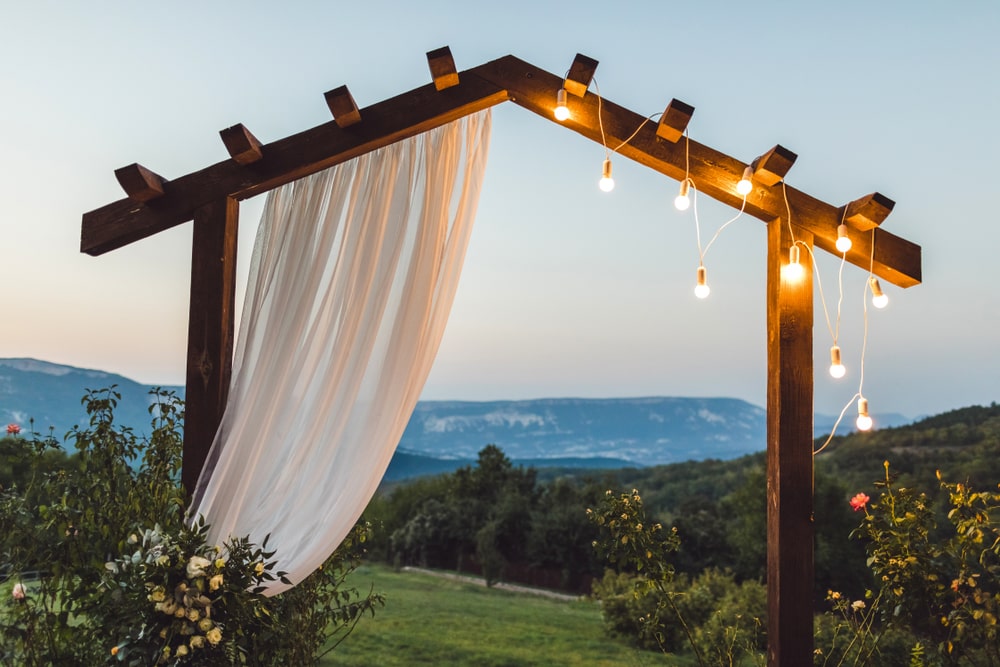 ooden wedding arch with white cloth and light bulbs outdoors with an amazing mountain view