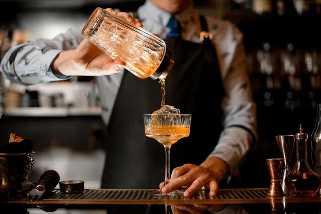 Barman gently pours a finished cocktail from a glass shaker into a glass