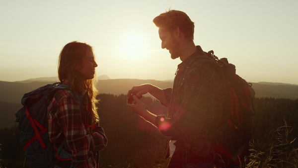 Male hiker making romantic proposing to woman in mountain landscape at sunset
