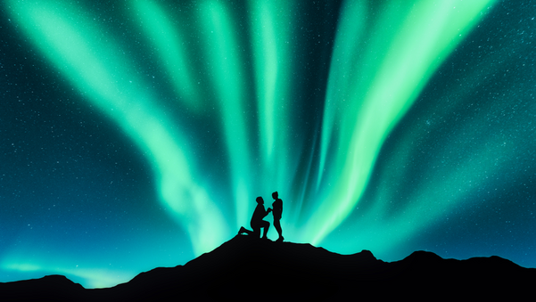 Northern lights and silhouettes of a man making marriage proposal to his girlfriend on the hill