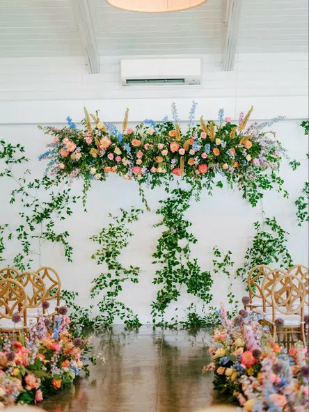 Colorful flower arch at the end of aisle lined with similar flowers and simple styled chairs
