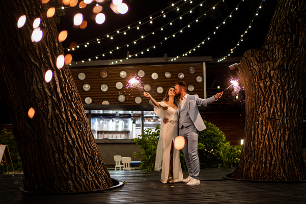 Newlyweds with sparklers in a night park with garlands on the trees