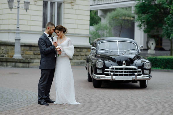 Happy wedding couple embracing near vintage car