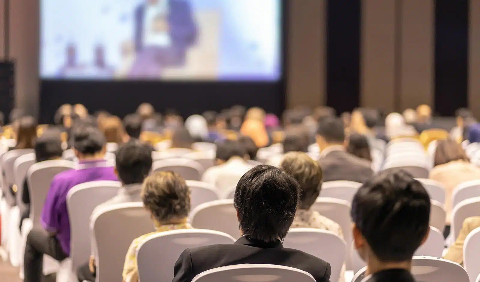Rear view of audience listening to speakers on the stage in a conference hall