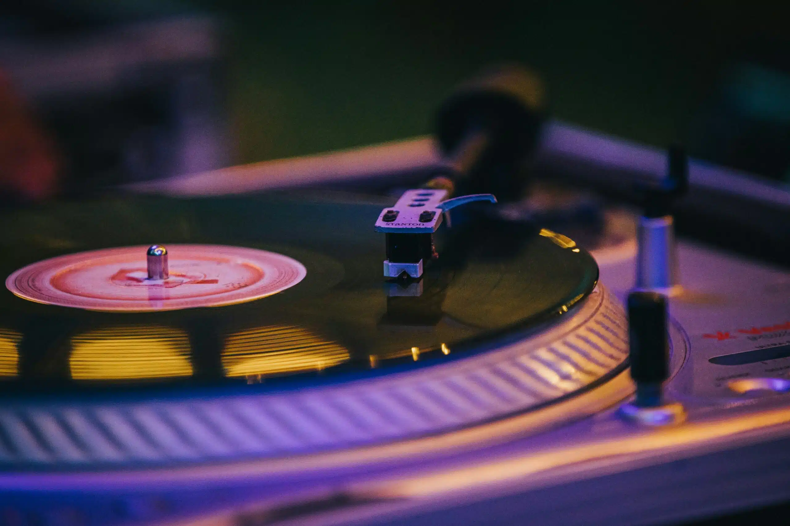 Close-up of a vinyl record on a turntable under colorful lighting, symbolizing advanced audio features that enhance the overall event experience.