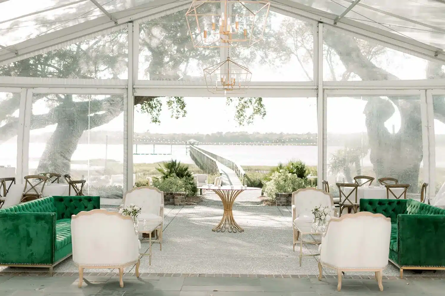 Elegant clear-top tent with statement chandelier, velvet lounge seating, and a waterfront view