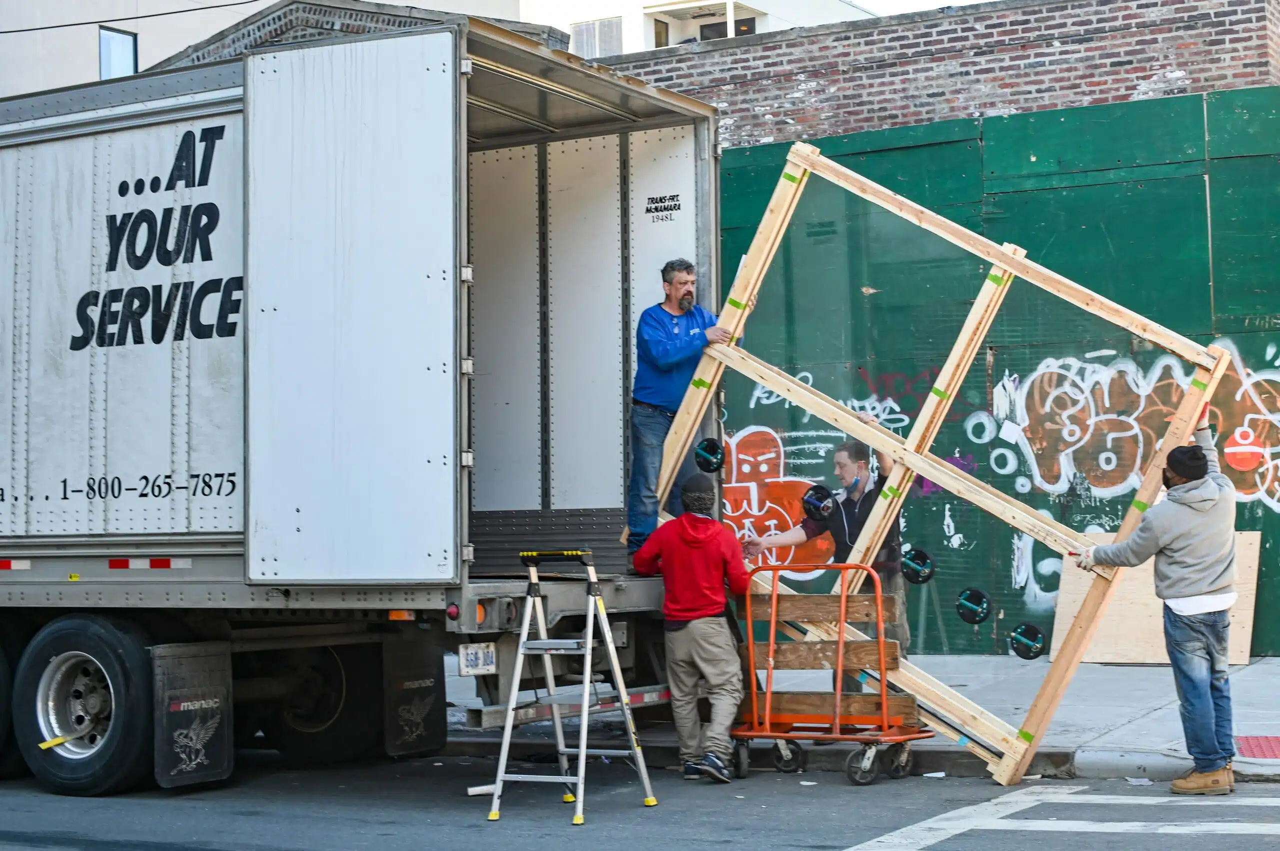 A team unloads large rental items from a truck, illustrating the behind-the-scenes coordination involved in managing designer wedding cocktail hour logistics. | Curated Events Crew members unloading event rental equipment from a delivery truck, ensuring smooth setup logistics for an outdoor celebration.
