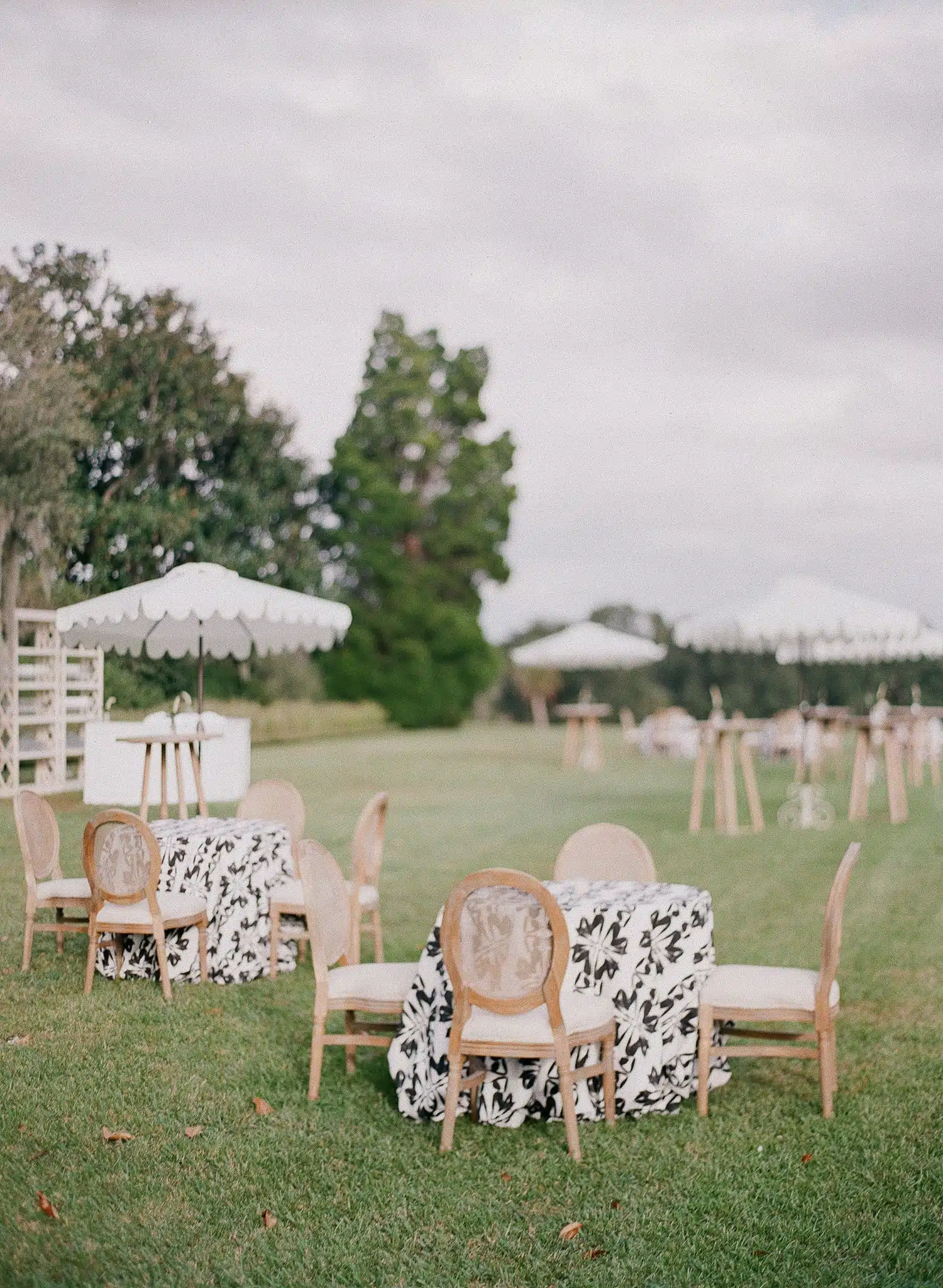 Outdoor lounge area with patterned table linens, vintage chairs, and scalloped umbrellas on a grassy lawn.