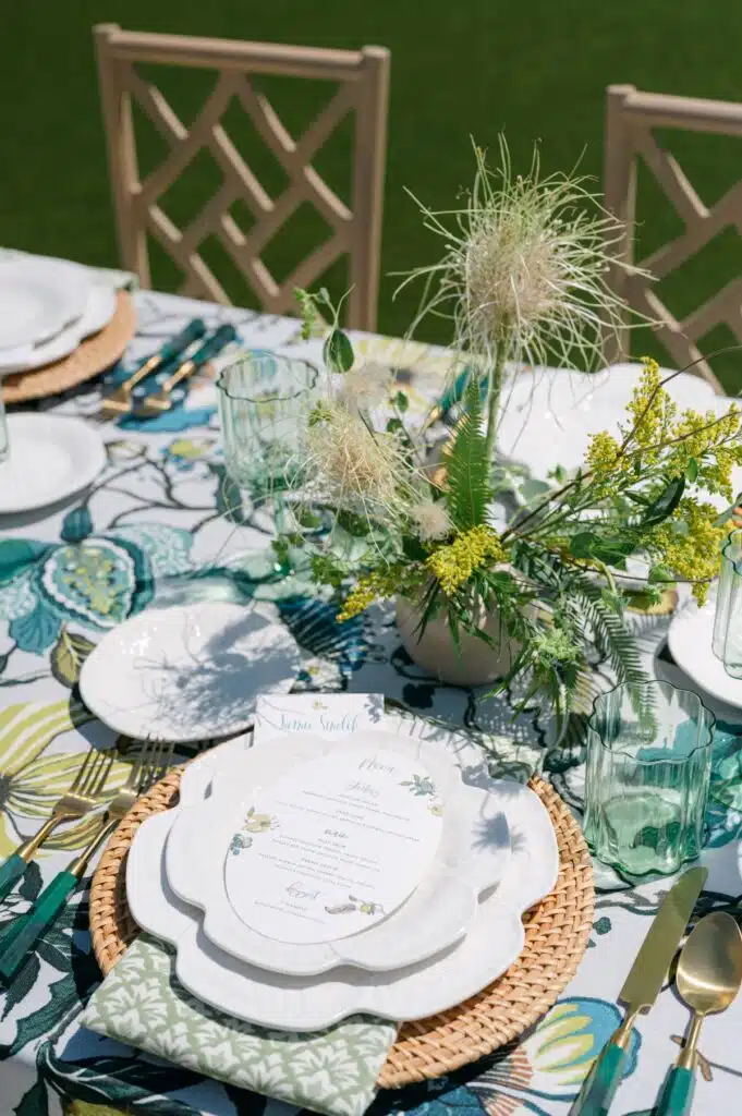 Close-up of outdoor place setting with scalloped plates, printed tablecloth, and wildflower-inspired centerpiece.