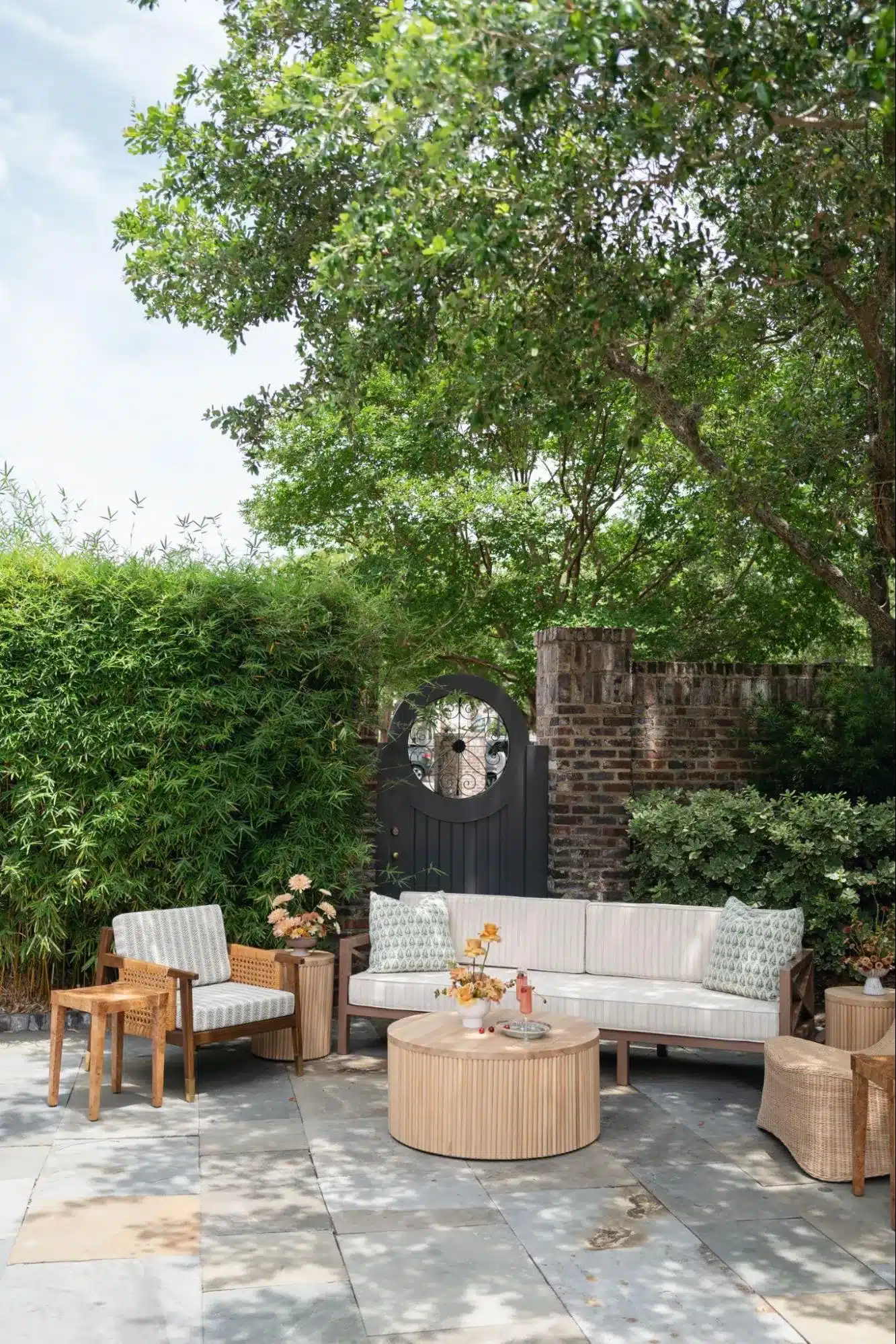 Outdoor garden lounge with modern wood and wicker seating surrounded by lush greenery and brick walls.