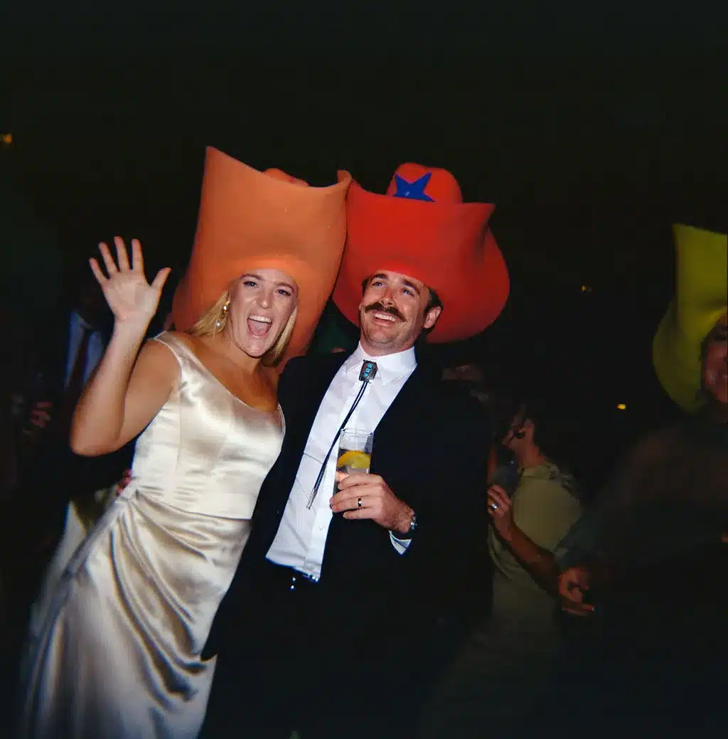 Couple wearing oversized cowboy hats dancing and posing for a fun party moment. | Curated Events Couple wearing oversized cowboy hats dancing and posing for a fun party moment.