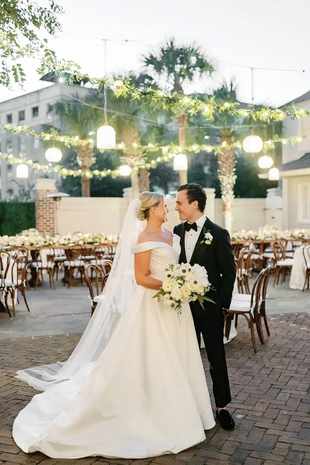 Newlyweds smiling at outdoor reception with round tables and string lights