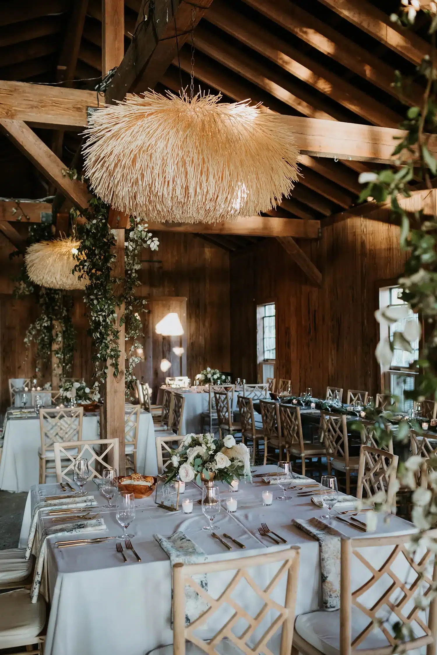 Elegant barn wedding reception with rattan chandeliers, neutral floral centerpieces, and wooden chairs | Curated Events Elegant barn wedding reception with rattan chandeliers, neutral floral centerpieces, and wooden chairs