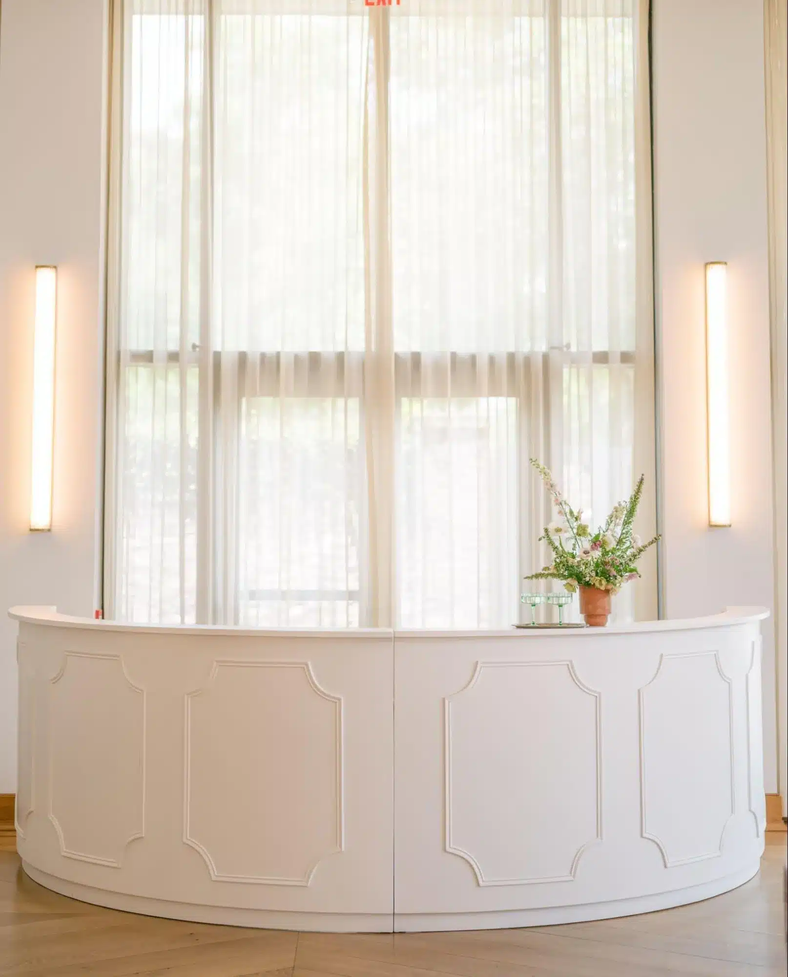 Designer curved white bar with paneled details, styled with a minimalist floral arrangement for a wedding event.