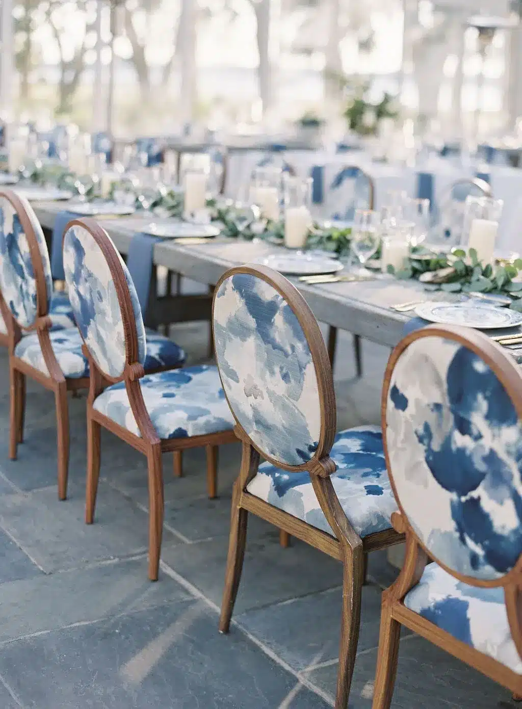 Long reception table with designer blue watercolor upholstered chairs and greenery garland runner.