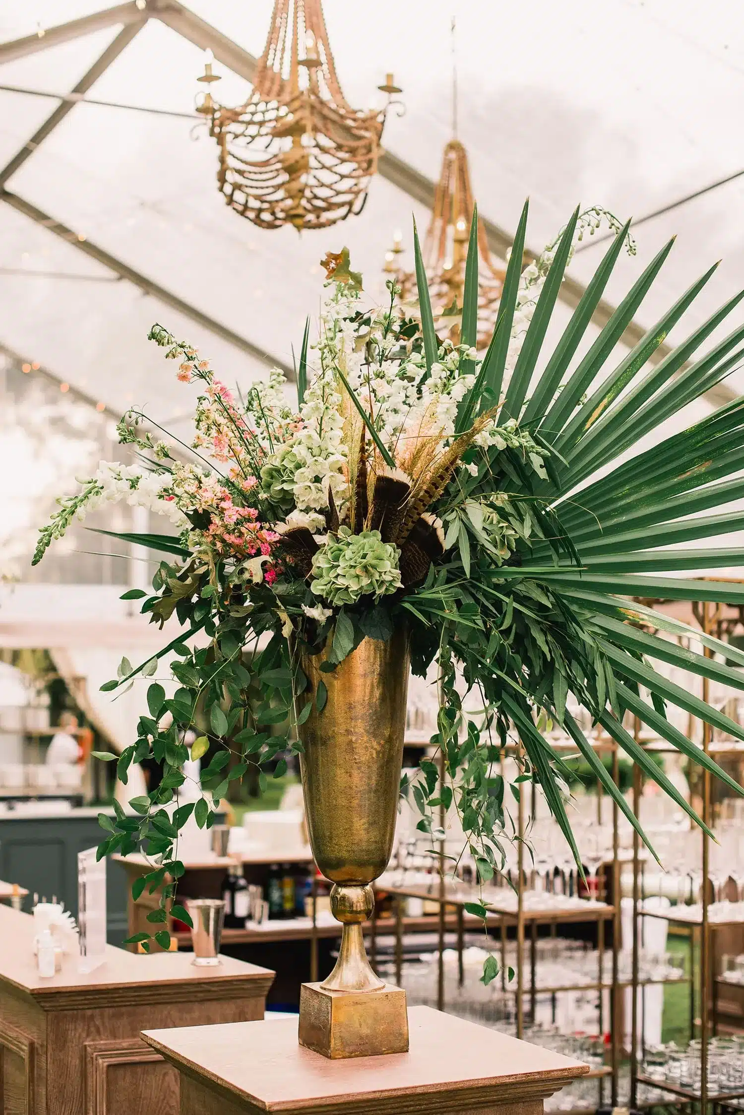 Statement tropical floral arrangement in a gold urn under a clear tent with beaded chandeliers. | Curated Events Statement tropical floral arrangement in a gold urn under a clear tent with beaded chandeliers.
