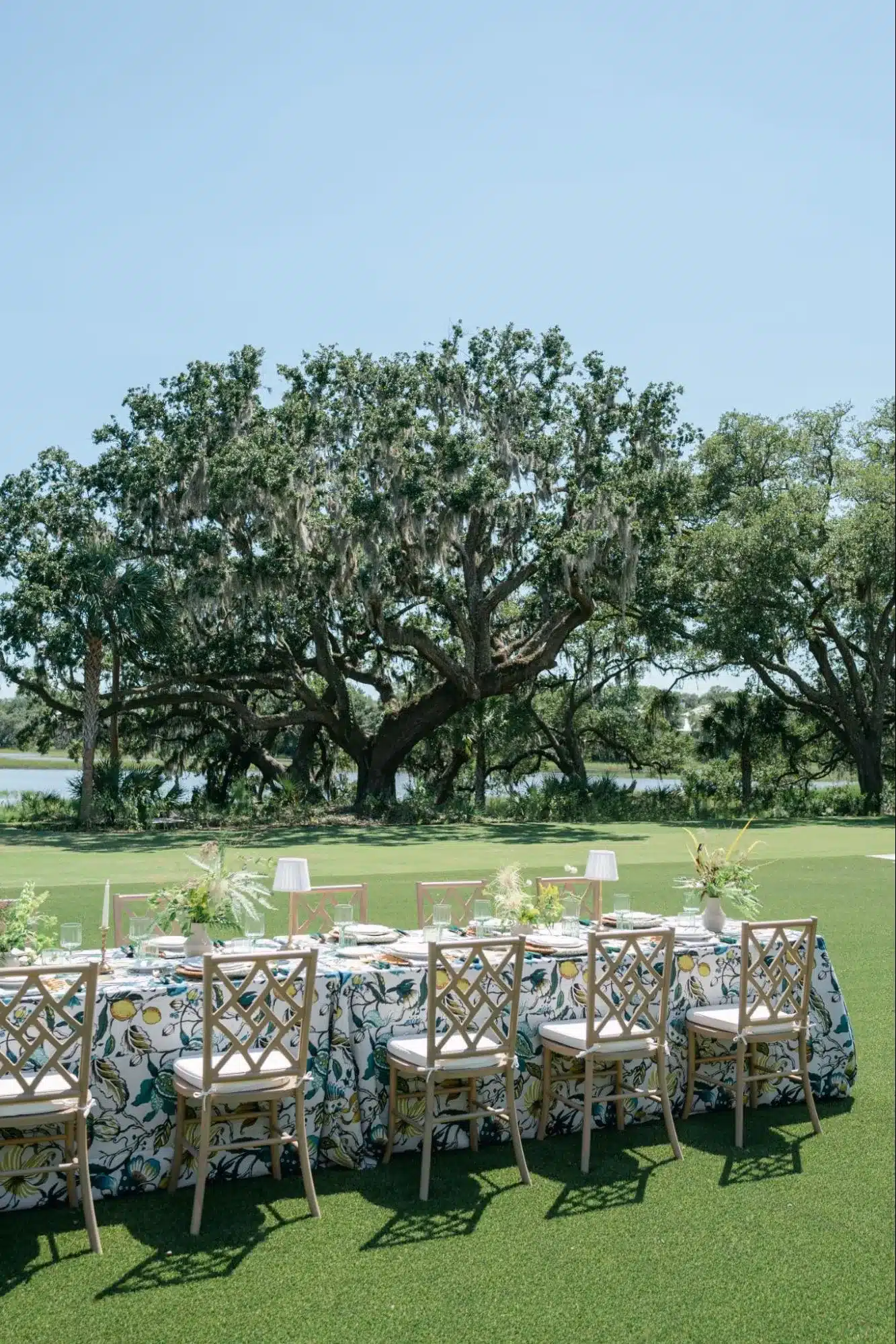 Outdoor wedding table with colorful fruit-patterned linens, cross-back chairs, and small white lamps | Curated Events Outdoor wedding table with colorful fruit-patterned linens, cross-back chairs, and small white lamps