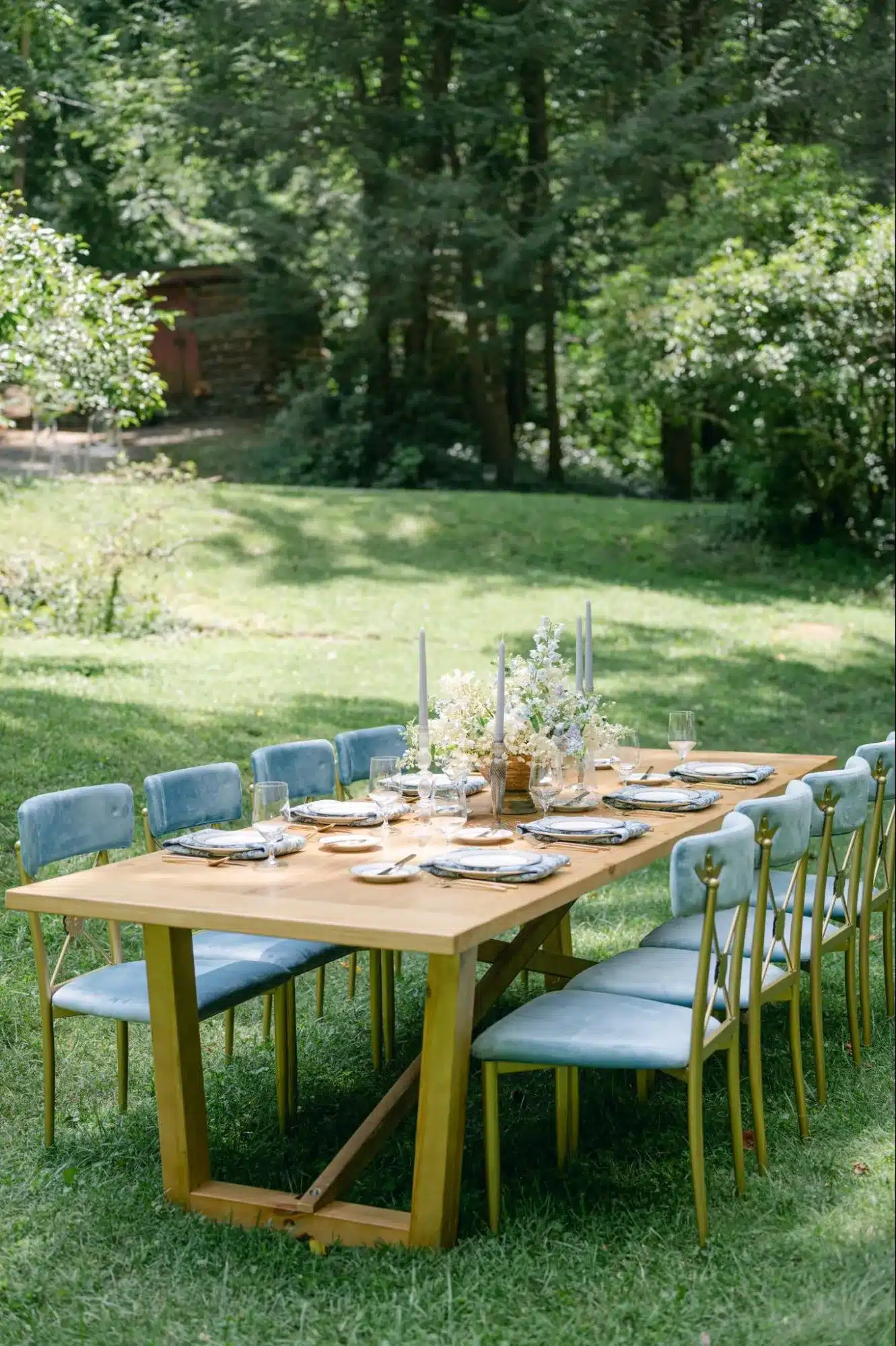 Rustic wood table with pastel blue chairs set for an intimate outdoor garden celebration.