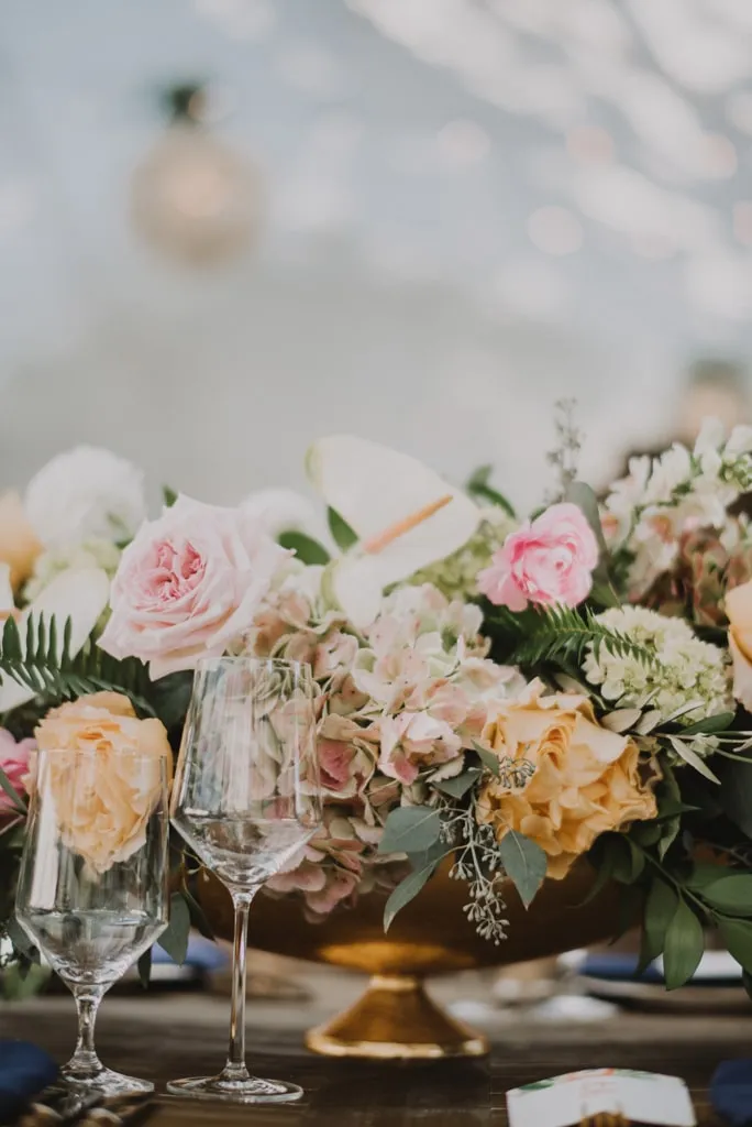 Close-up of a lush floral centerpiece with roses and hydrangeas in a gold bowl.