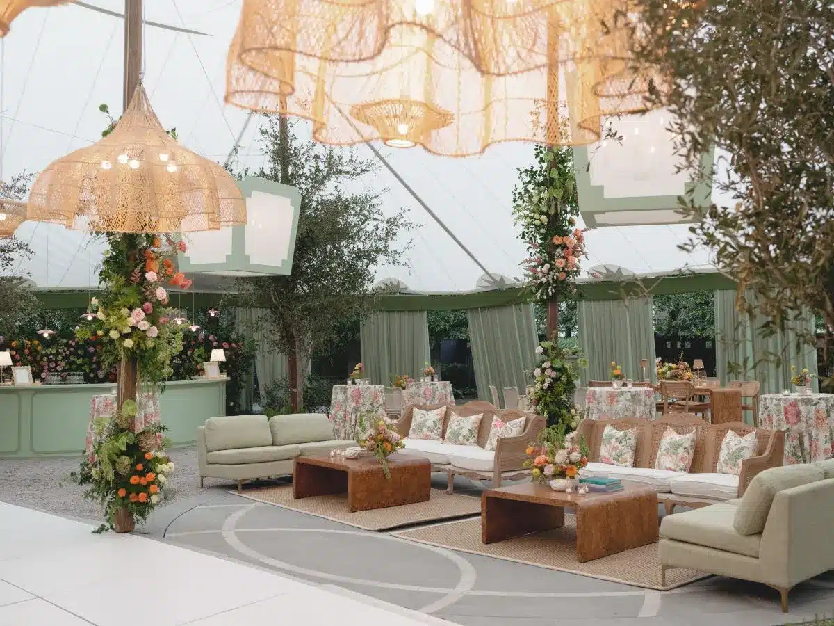 Boho-inspired tented lounge with rattan chandeliers, green draping, and floral accents.