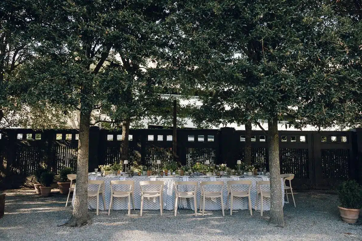 Outdoor banquet table under trees with neutral seating and garden-inspired linens.