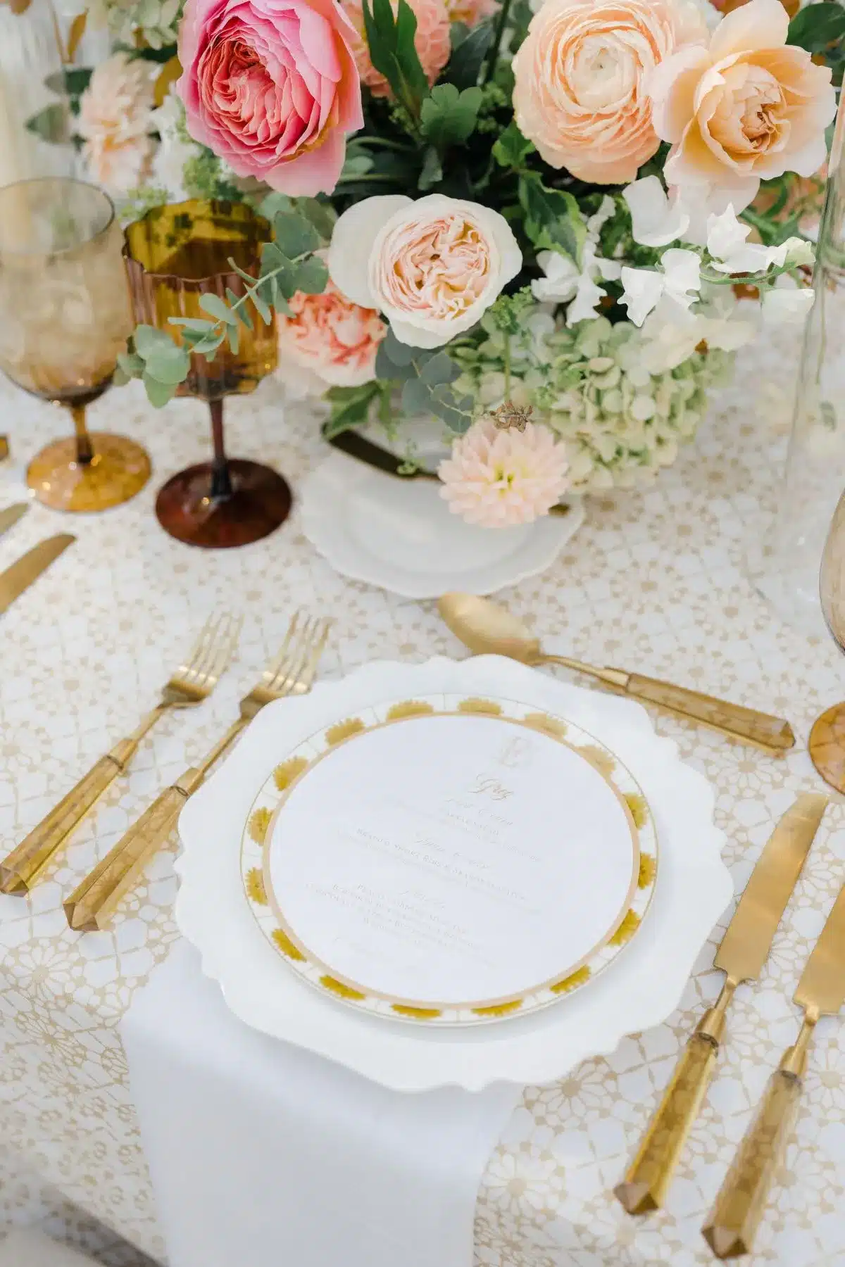 Elegant wedding place setting with gold flatware, floral china, and pastel centerpiece.