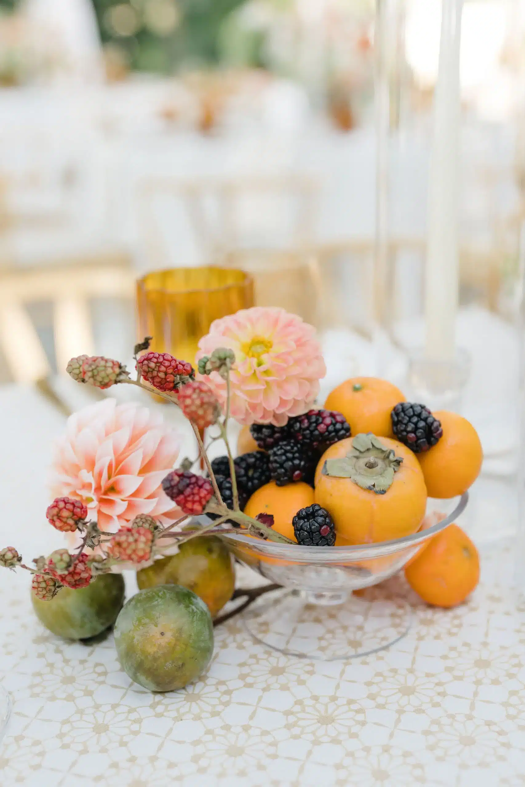 Decorative bowl with persimmons, blackberries, figs, and pink dahlias on a patterned tablecloth