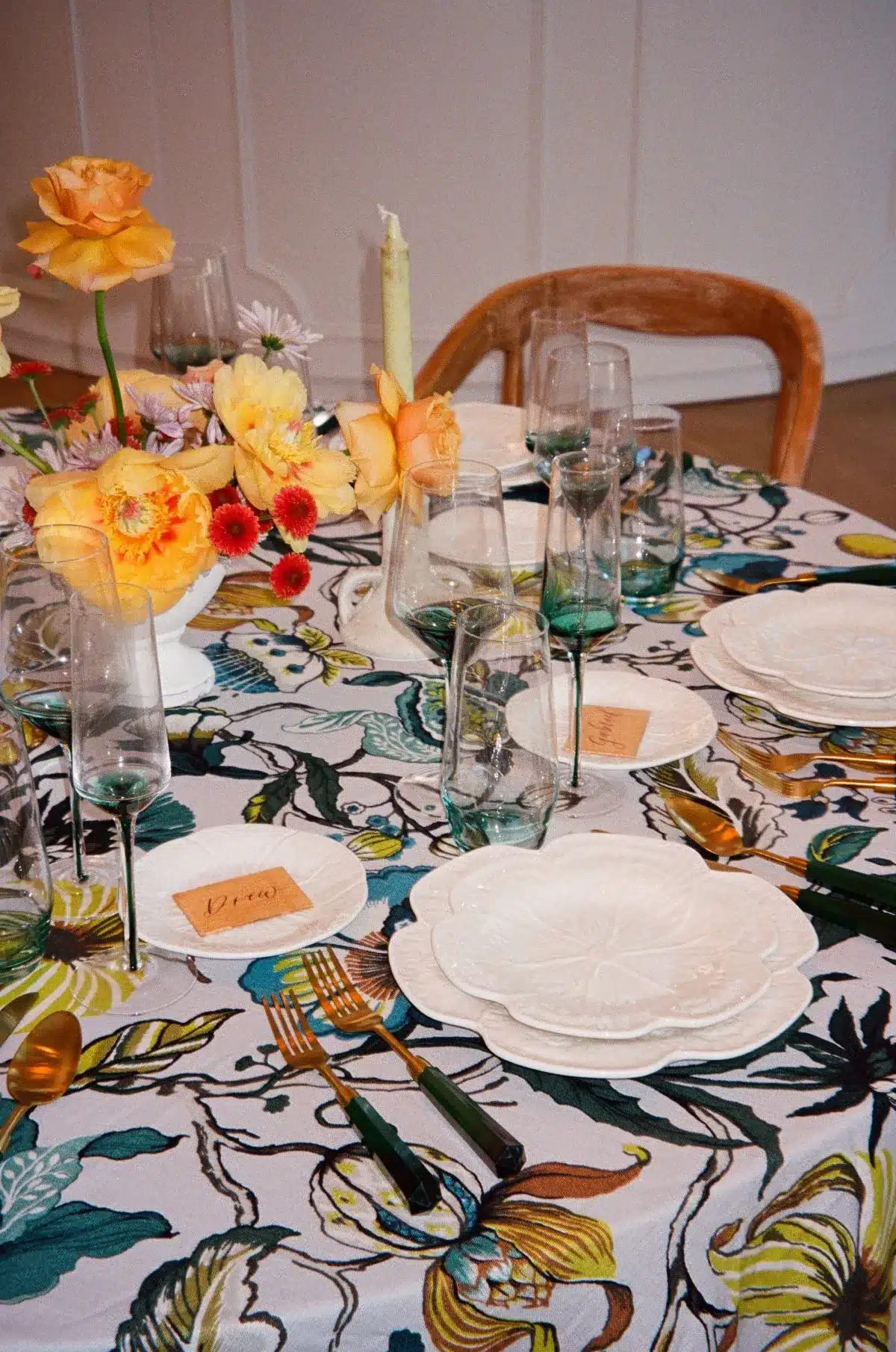 Vibrant floral tablecloth with white plates, colorful flowers, and green-tinted glassware.