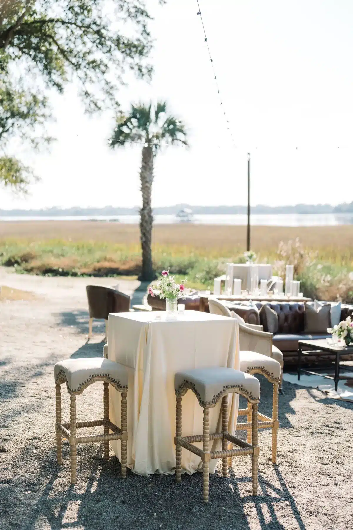 Cocktail table with neutral linens and bar stools at outdoor event. | Curated Events Cocktail table with neutral linens and bar stools at outdoor event.