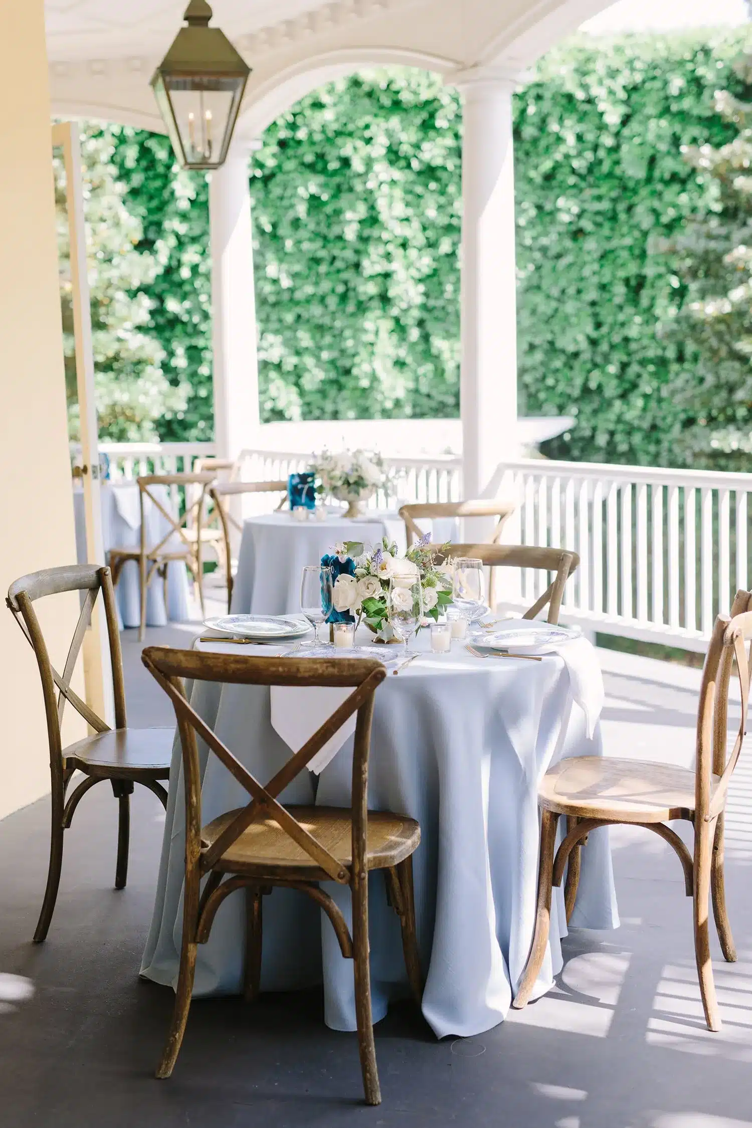 Covered-porch reception table with light blue linens, wooden chairs, and a white-and-blue floral centerpiece