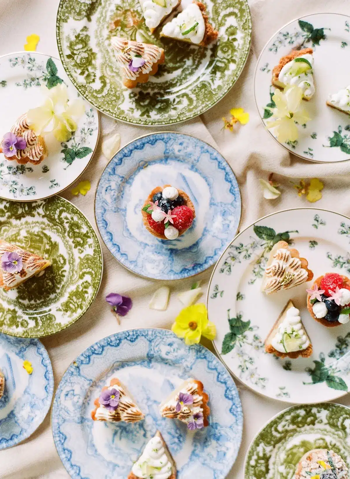 Holiday dessert display with assorted mini cakes on vintage green and blue patterned plates.