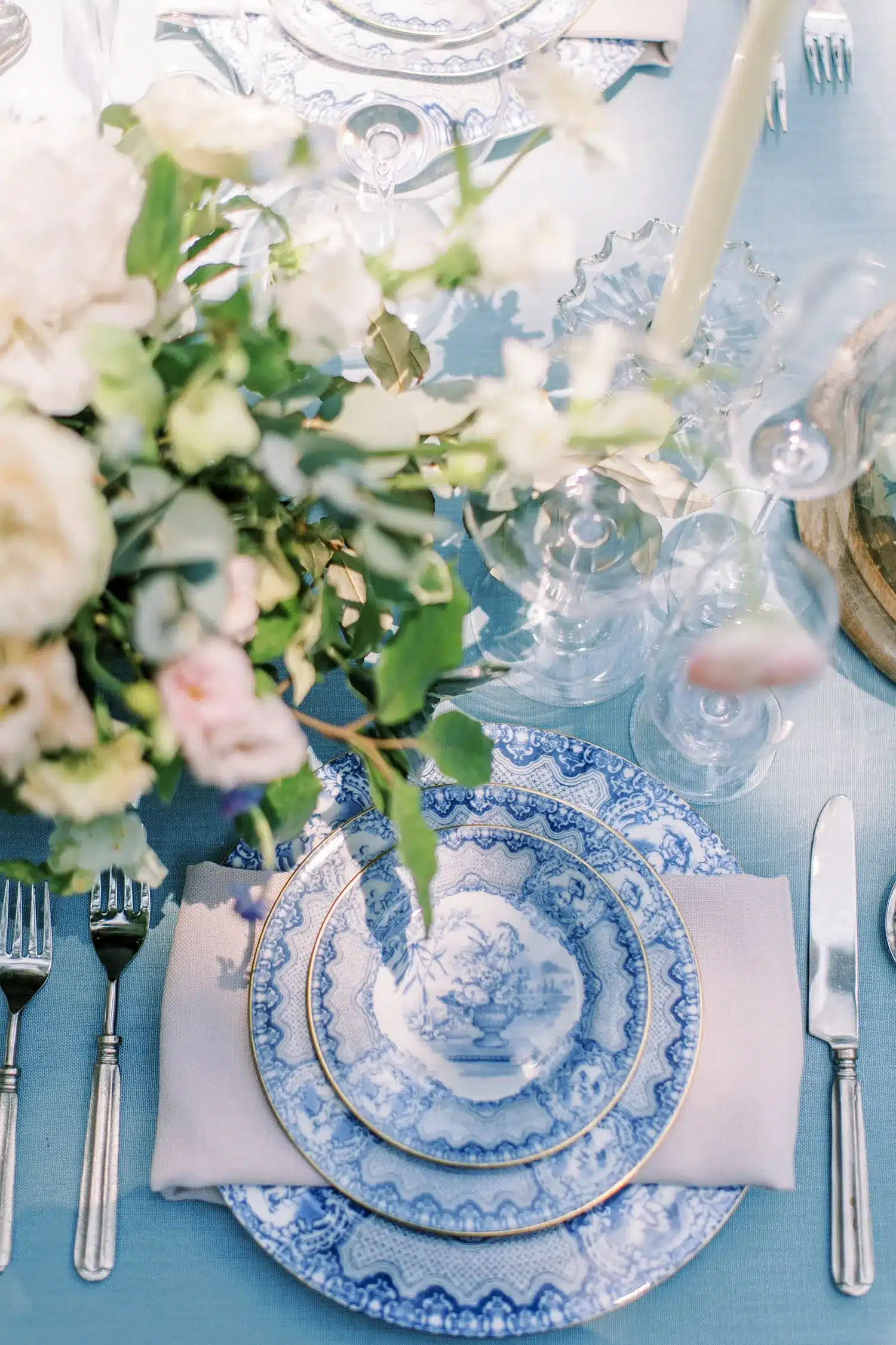 Elegant blue and white china place setting with floral centerpiece and glassware.