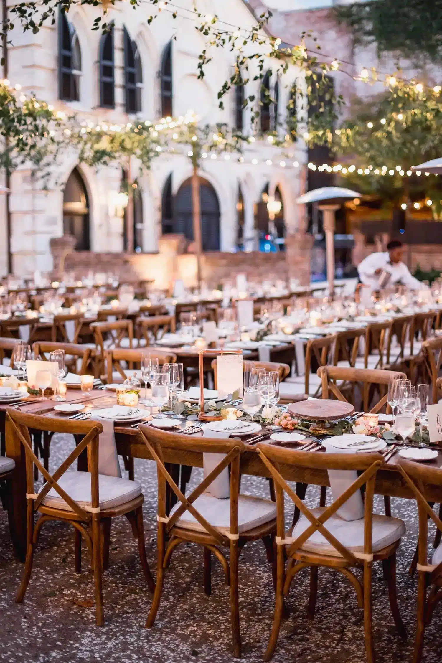 Outdoor holiday dinner setting with string lights, greenery garlands, and candlelit tables
