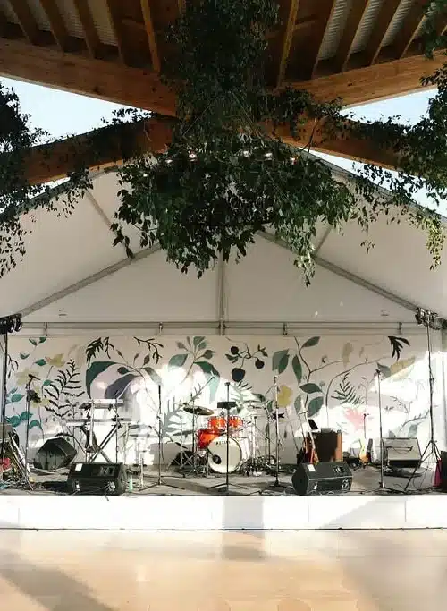 Outdoor stage setup under a tent with musical instruments and greenery d&eacute;cor.