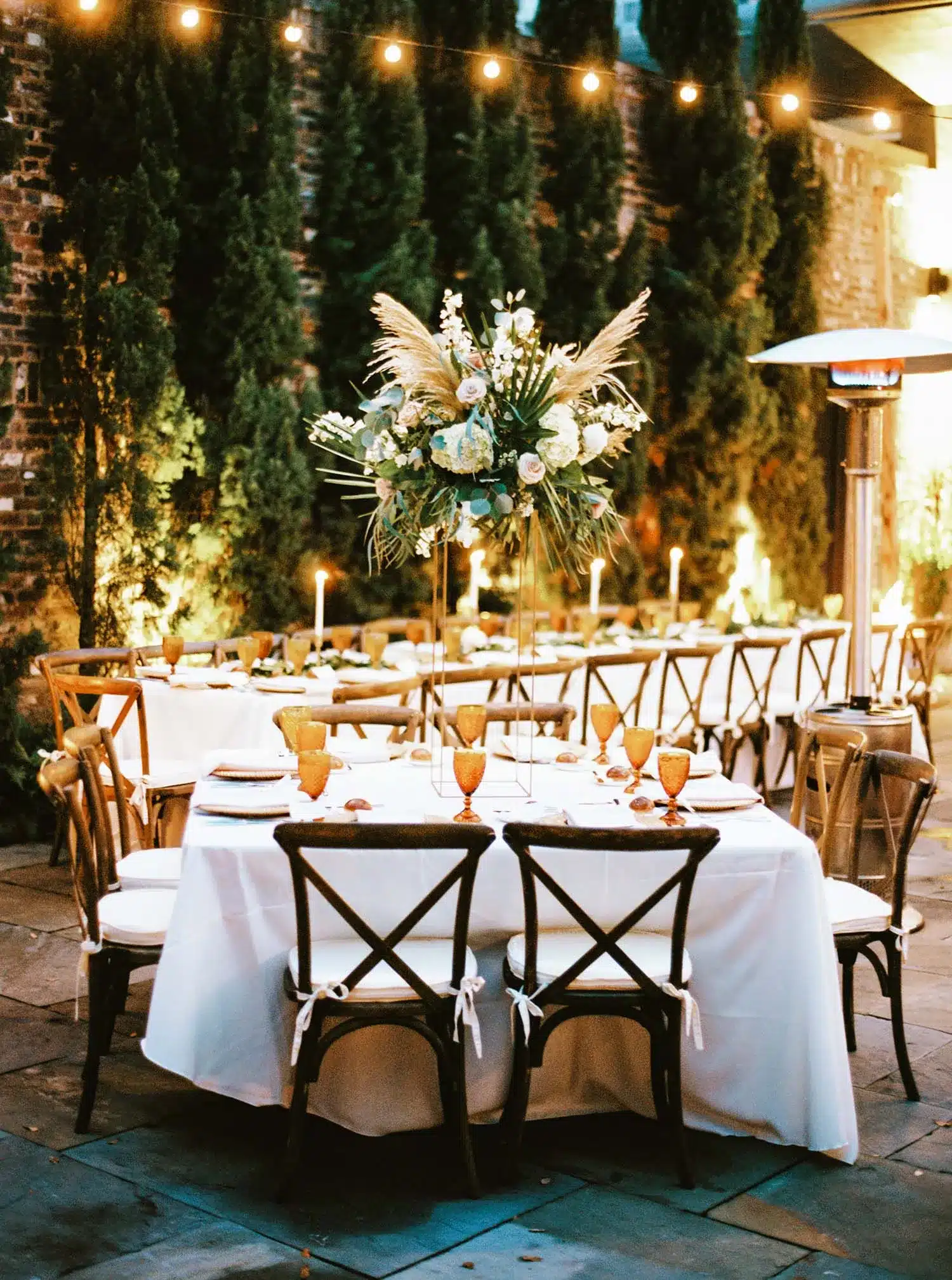 Outdoor holiday tablescape with tall floral arrangements, amber glassware, and warm candlelight