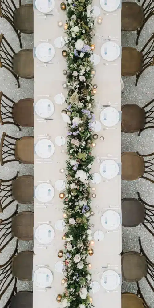 Aerial view of a long dinner table with elegant floral garland and candlelit place settings for a Raleigh holiday event.