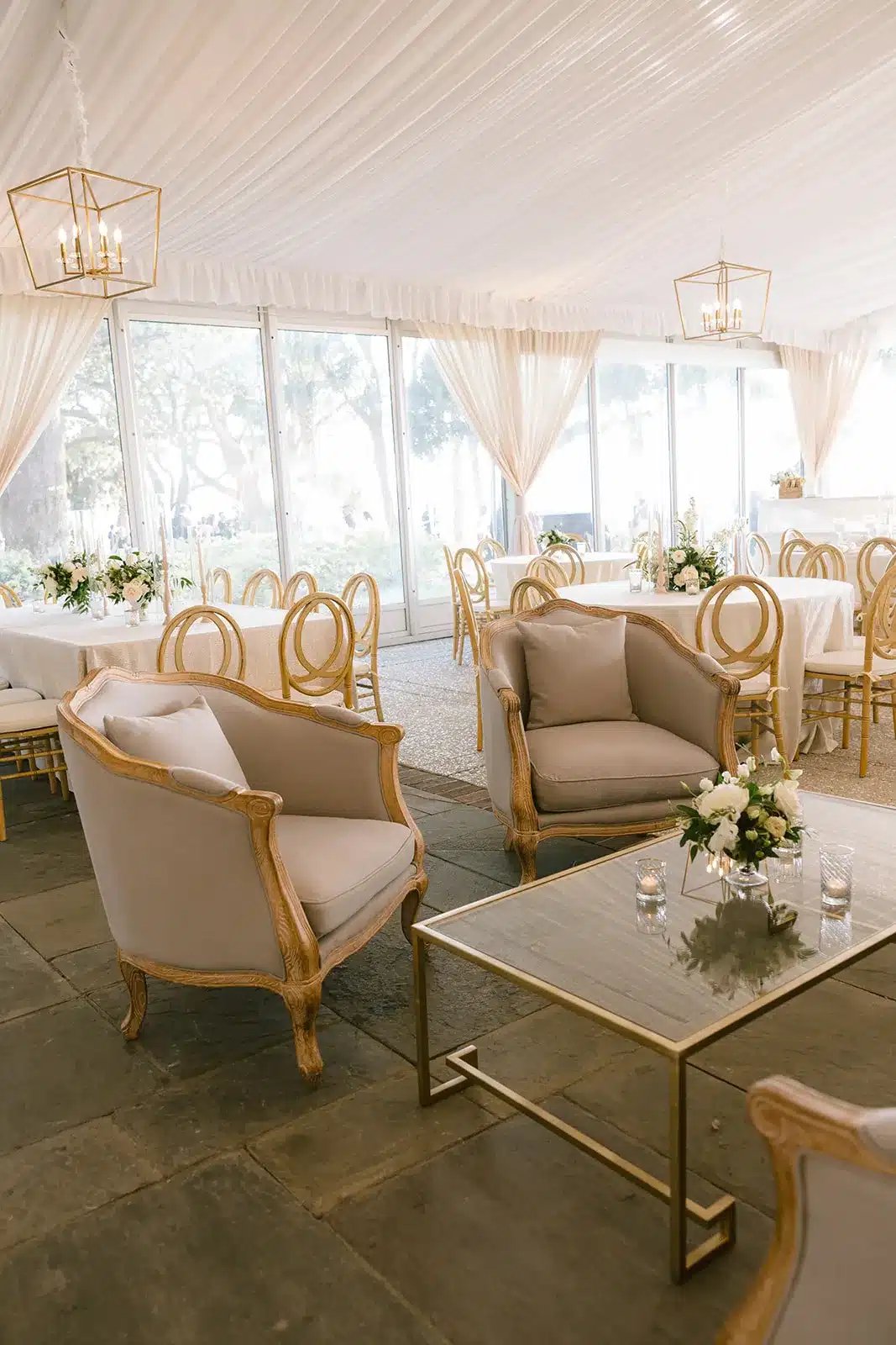 Draped tent interior with soft white fabric ceiling, gold chandeliers, and natural light streaming through sidewalls.