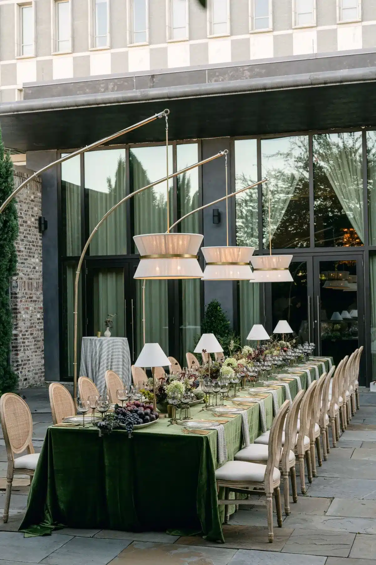 Outdoor holiday dinner setup with green velvet tablecloths, rattan chairs, and hanging pendant lights in Raleigh.
