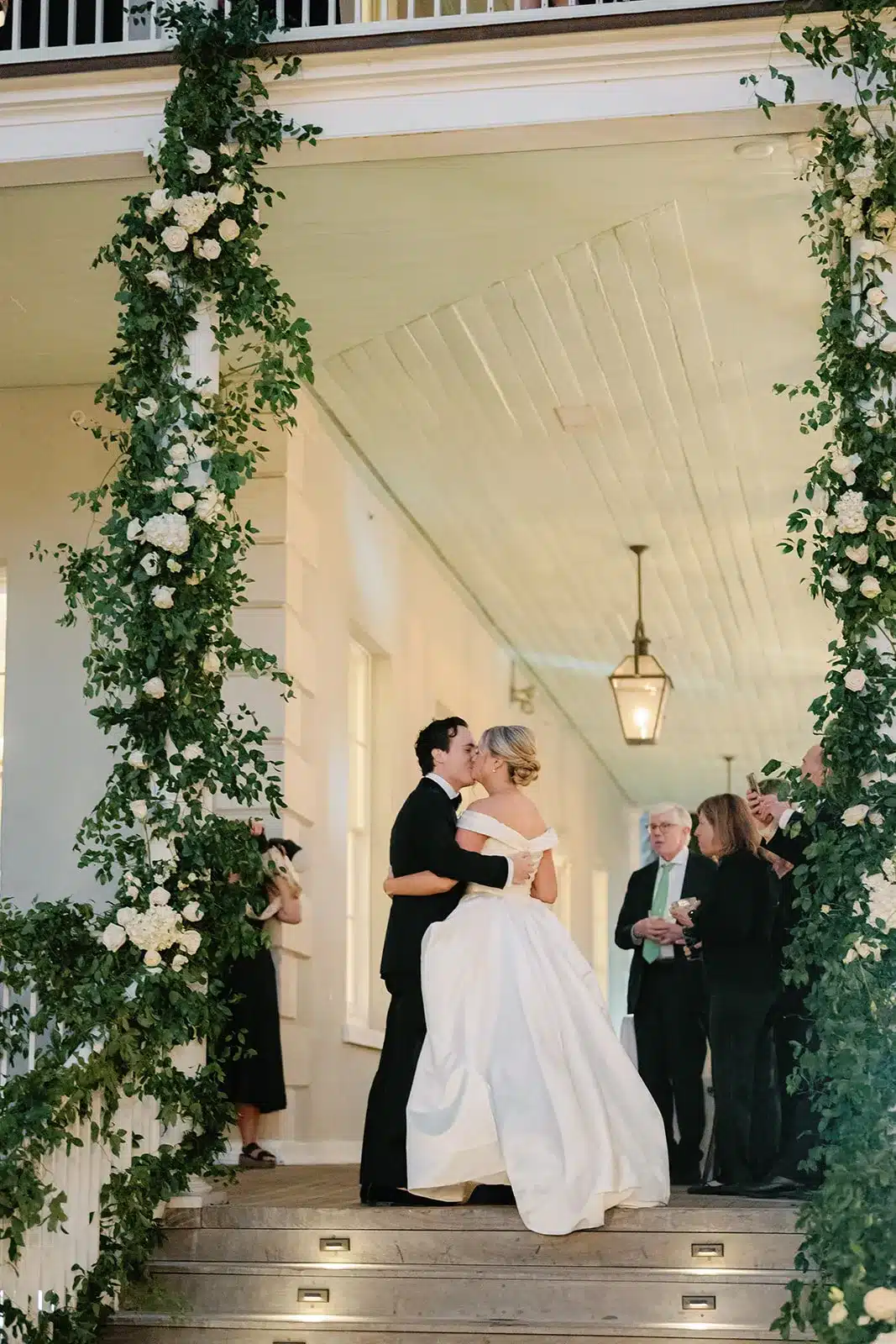 Bride and groom sharing a kiss on a flower-adorned porch.