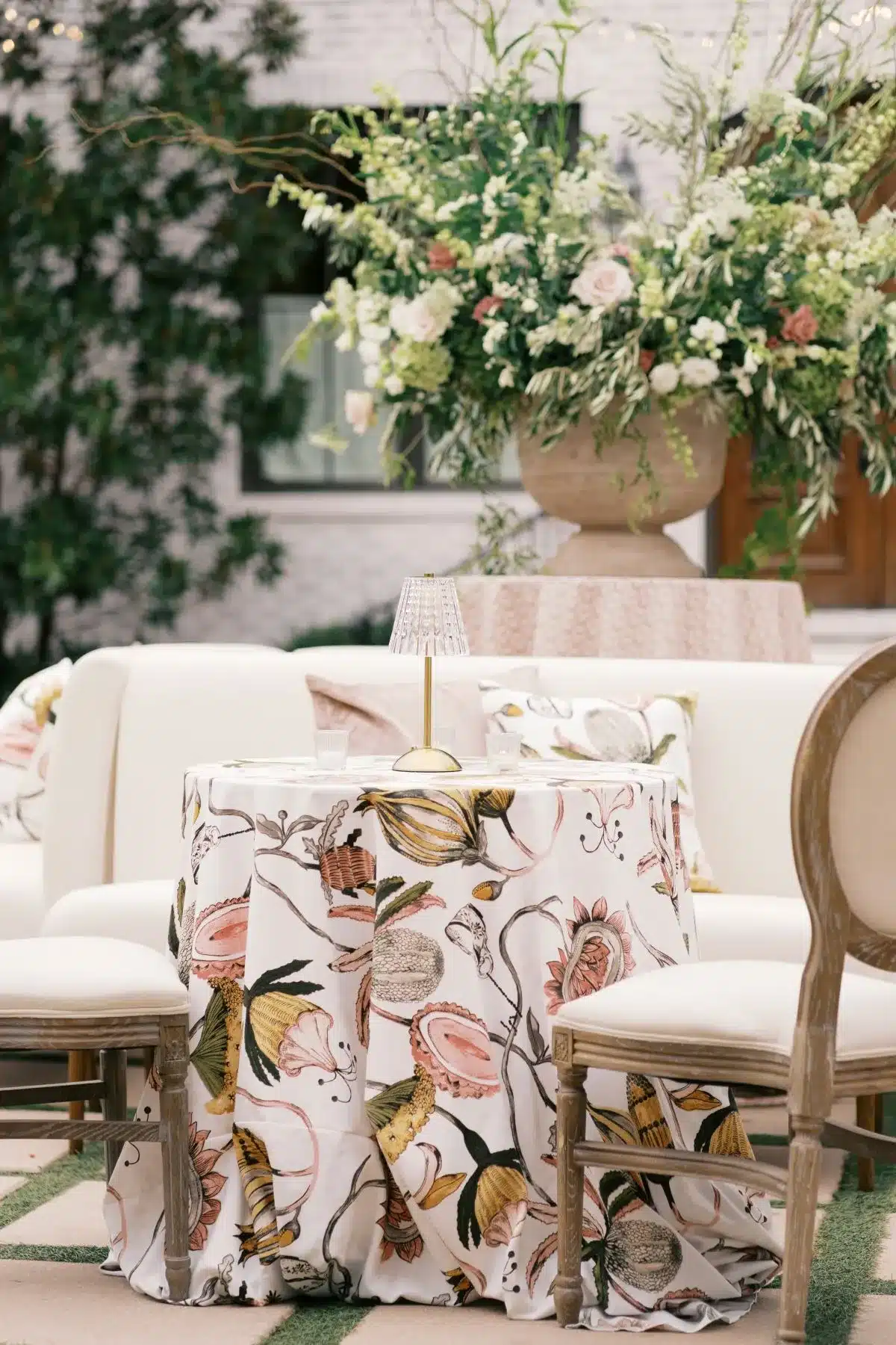 Lounge vignette with botanical-print linens, soft blush seating, and lush green florals.