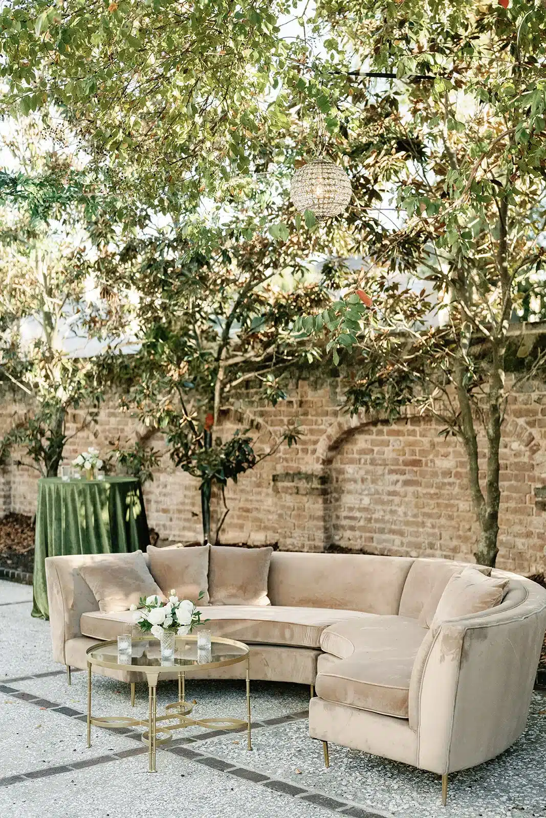 Curved beige sectional with gold nesting tables in a brick courtyard lounge area.