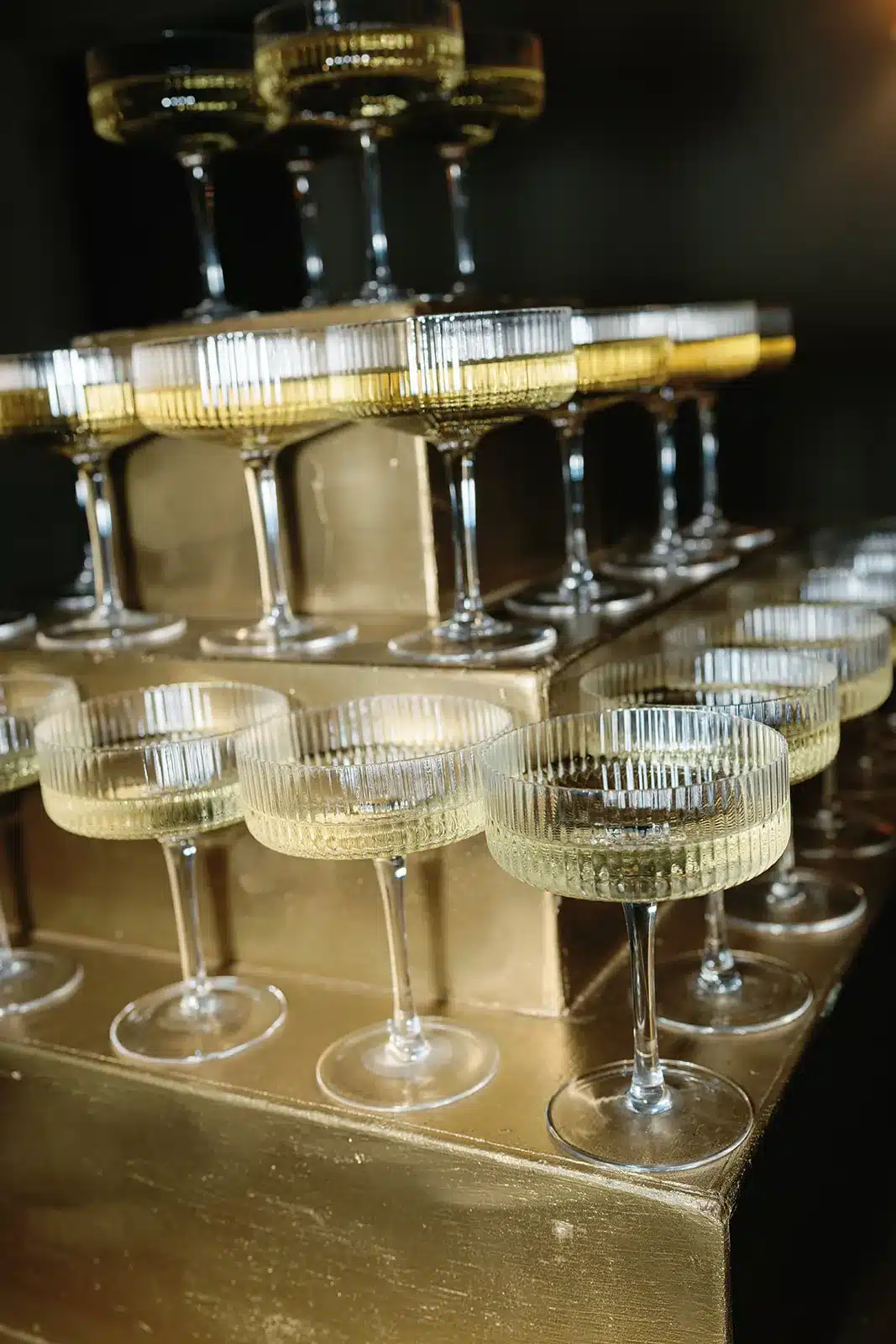 Tiered display of coupe glasses on a gold stand for a luxury cocktail presentation.