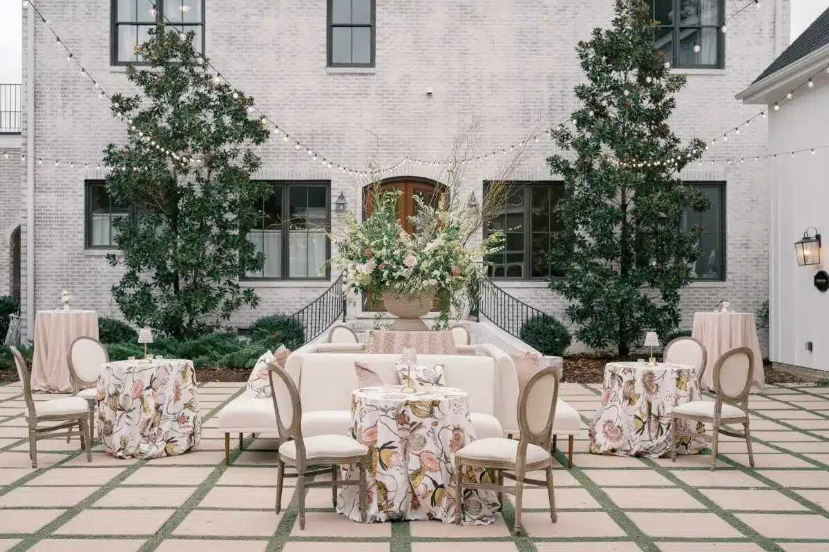 Elegant outdoor event setup featuring floral-patterned tables, white lounge seating, and a lush floral arrangement, ideal for Charleston weddings and corporate events.