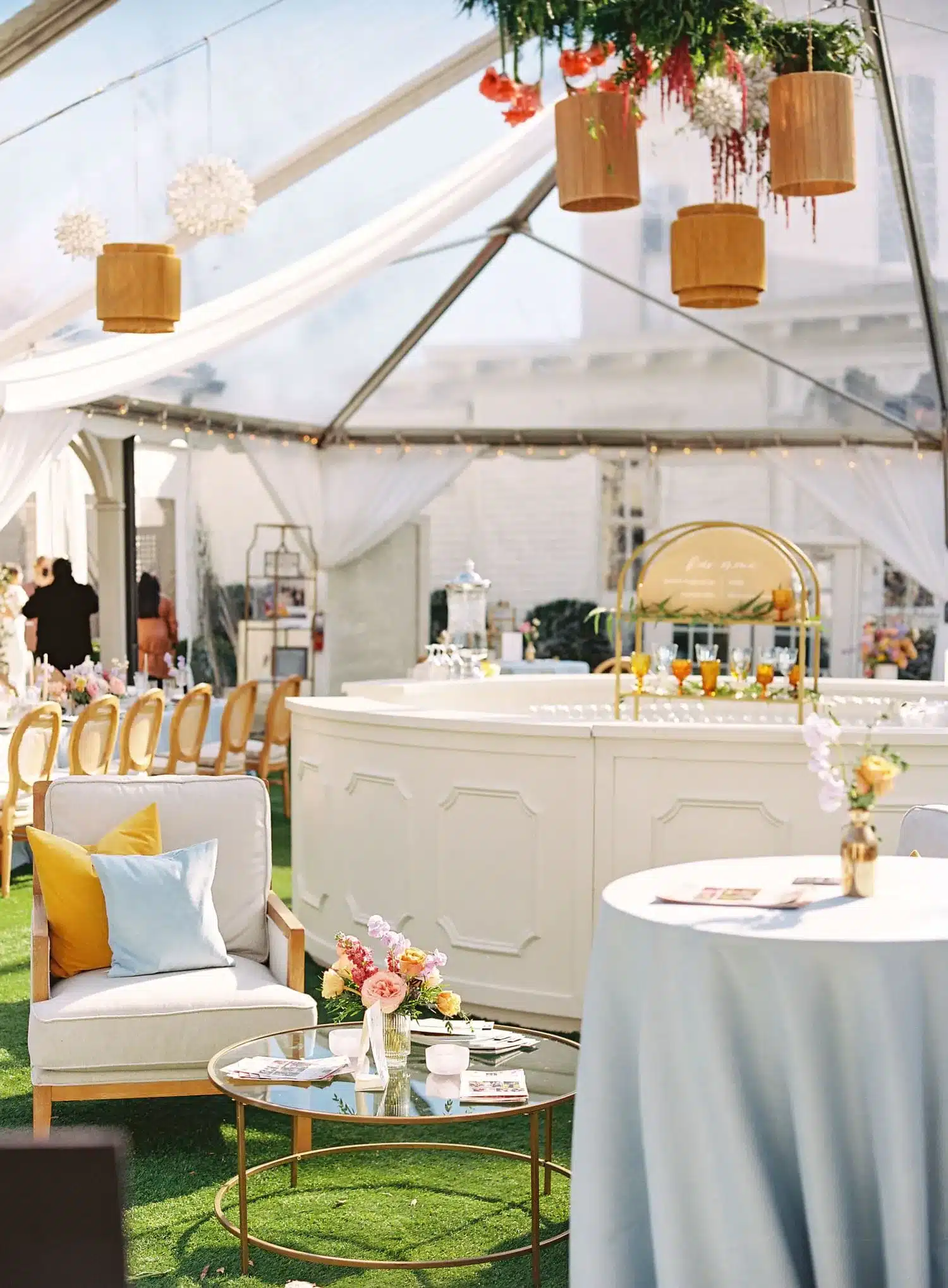White wedding bar inside a clear-top tent with lounge seating and floral accents.