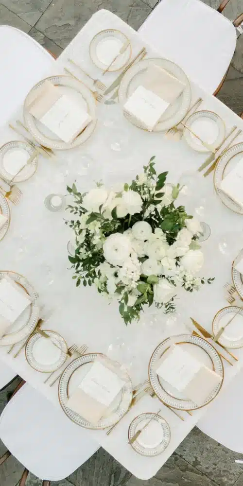 Round table setting with white floral centerpiece and gold-rimmed dinnerware.
