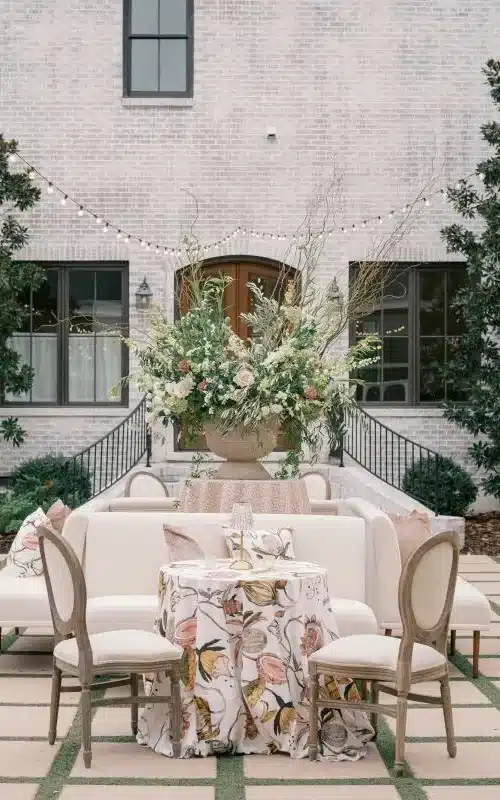 Courtyard lounge with floral linens, upholstered seating, and string lights overhead.