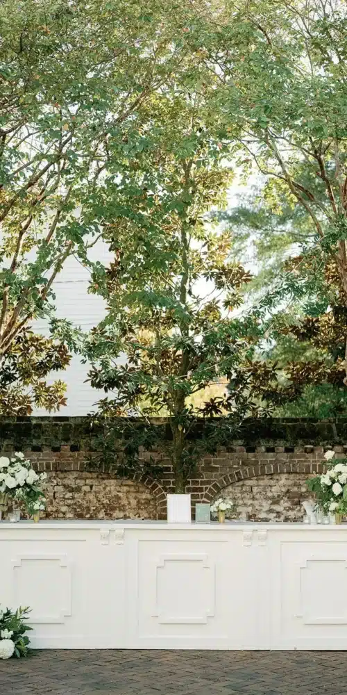 White wedding bar with floral arrangements set against a brick wall in an outdoor Savannah venue.