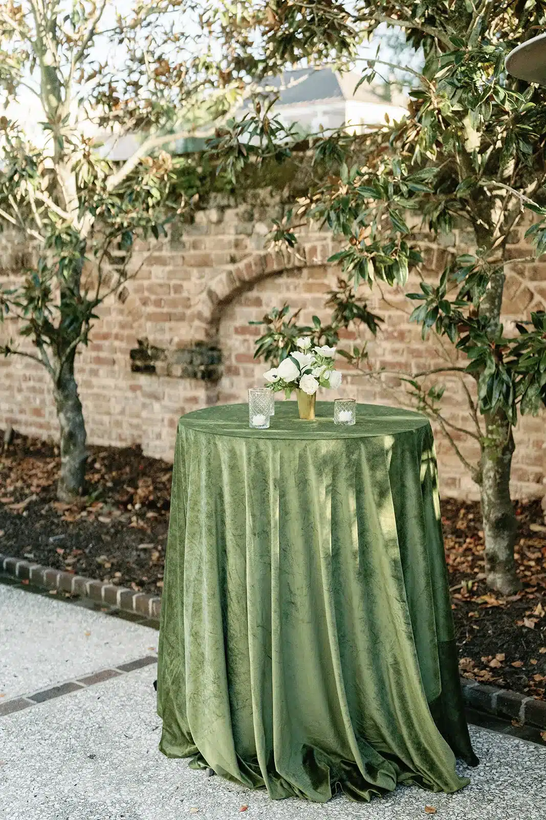 Velvet green cocktail table styled with petite floral arrangement against a brick wall.